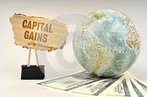 On a gray surface, a globe, dollars and a cardboard plate with the inscription - Capital Gains