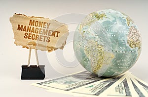 On a gray surface, a globe, dollars and a cardboard plate with the inscription - Money Management Secrets