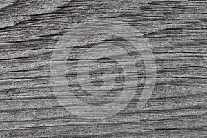 The gray surface of an old weathered wooden board. Horizontal wavy pattern of annual rings. Dark background or wallpaper. The