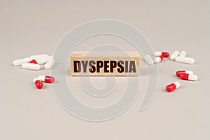 On a gray surface are tablets, capsules and a wooden plate with the inscription - Dyspepsia