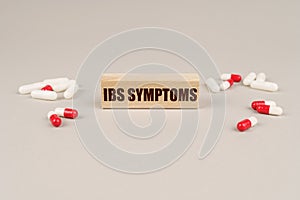 On a gray surface are tablets, capsules and a wooden plate with the inscription - IBS Symptoms