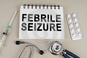 On a gray surface there is a syringe, a stethoscope and a notepad with the inscription - Febrile seizure