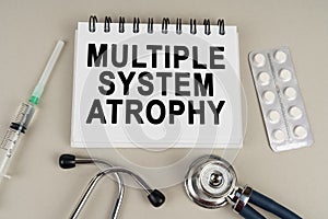 On a gray surface there is a syringe, a stethoscope and a notepad with the inscription - Multiple system atrophy