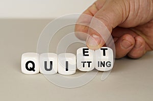 On a gray surface are white cubes with the inscription - QUIET or QUITTING