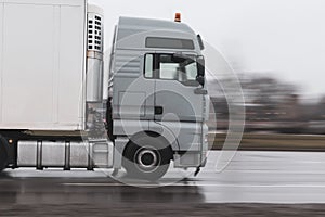 A gray truck in the rain pulls a semi-trailer on wet asphalt close-up. Motion blur