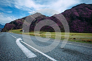 Gray two-lane road with stripes and arrow on the background of mountains. Asphalt pavement of a two-lane highway