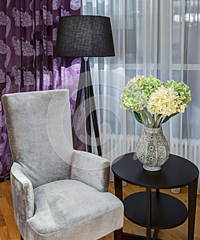 Gray velor armchair near rounded table.