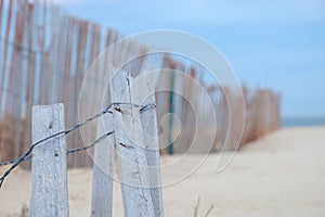 Gray and weathered storm fence slowly being covered by sand dune