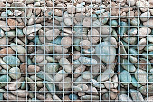 Gray white and blue round stones in metal mesh background. Natural environmental material fencing.