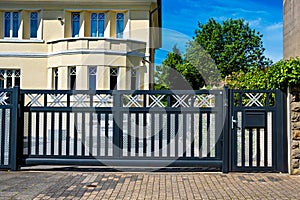 A gray and white metal gate with a brick walkway in front of the house in Germany