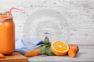 A gray wooden table with a board, mason jar full of carrot smoothie with basil, orange and mint on a blurred background.