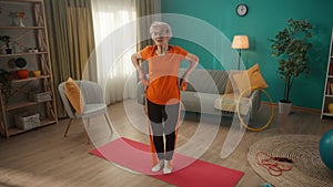 A grayhaired retired woman works out in the living room with a sports elastic band. An elderly woman, stepping on the