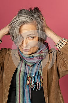 Graying mature woman making hairstyle, correcting her hair by hands. Creative lady gathered hair on back of her head