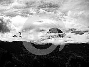 Grayscale aerial view of a mountain summit covered with clouds on a sunny day