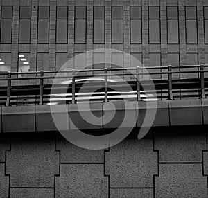 Grayscale of a car driving fast on a bridge