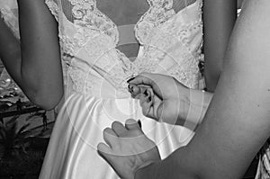 Grayscale closeup shot of a someone zipping up a woman's wedding dress