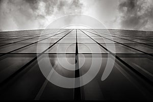 Grayscale low angle shot of a skyscraper a wall with glass windows under the cloudy sky