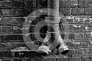 Grayscale of an old rain spigot in an alley with a wall background