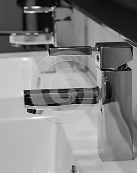 Grayscale shot of a bathroom interior with a hrome faucet and a white sink