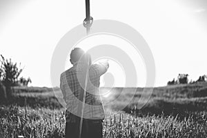 Grayscale shot from behind of a male carrying a wooden cross in a grassy field