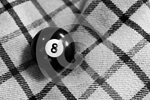 Grayscale shot of a billiard ball number 8 on a checkered fabric