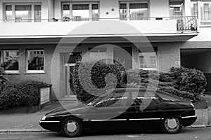 Grayscale shot of a black car parked in front of a residential building