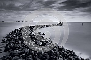 Grayscale shot of breakwater on water under a stormy sky above