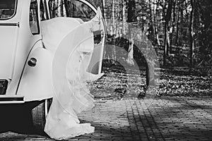 Grayscale shot of a bride's feet out from the retro car in the garden