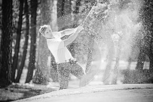 Grayscale shot of a Caucasian male golfer teeing off from a golf tee on a bright sunny day