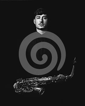 Grayscale shot of a cool and handsome guy holding his saxophone on a dark background