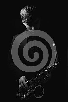 Grayscale shot of a cool and handsome guy holding his saxophone on a dark background