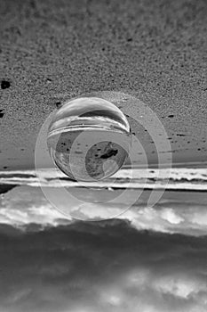 Grayscale shot of a crystal ball with the reflection of the sandy beach, the sea and cloudy sky