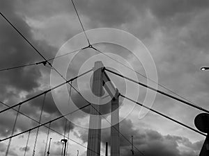 Grayscale shot of electric lines and cable bridge with a cloudy sky over it in Budapest