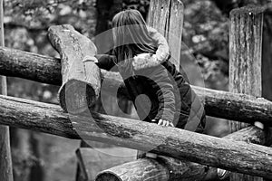 Grayscale shot of a girl standing next to a stack of logs.