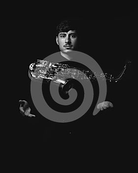 Grayscale shot of a handsome guy tossing into the air his saxophone isolated on a dark background