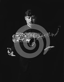 Grayscale shot of a handsome guy tossing into the air his saxophone isolated on a dark background