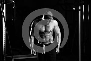 Grayscale shot of a healthy young Caucasian man posing in the gym and flexing his muscles