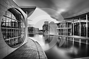 Grayscale shot of a lake in the middle of city buildings under a cloudy sky