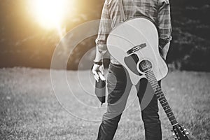 Grayscale shot of a lonely male with a guitar holding the Christian hymn book