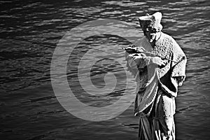 Grayscale shot of a male statue carrying the cross near the sea