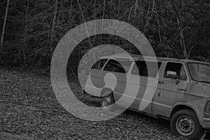 Grayscale shot of an old abandoned van near trees in a forest