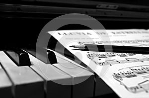 Grayscale shot of a piano with sheet music and pencil