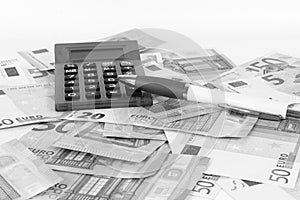 Grayscale shot of a pile of money with a calculator and a ballpen on top
