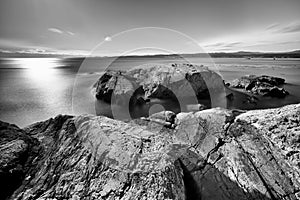 Grayscale shot of rocks surrounded by the sea with long exposure in Esquimalt, Vancouver, Canada