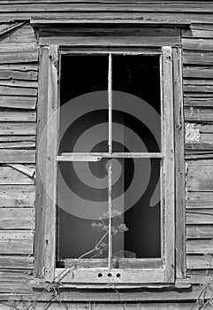 Grayscale shot of a rusty broken window in old wooden wall, vertical shot