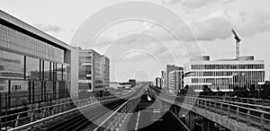 Grayscale shot of train tracks in the middle of buildings with a cloudy sky in the background