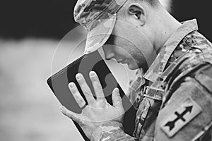 Grayscale shot of a young soldier praying while holding the bible