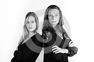 Grayscale studio shot of two Caucasian women standing back to back with a white background