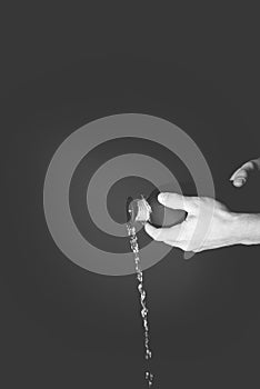 Grayscale vertical shot of a person pouring water out of a black bottle photo