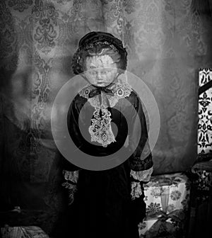 Grayscale of a vintage doll in front of a wall with an ornamental pattern